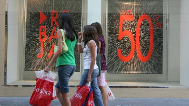 Unas jóvenes pasean junto a un comercio en rebajas